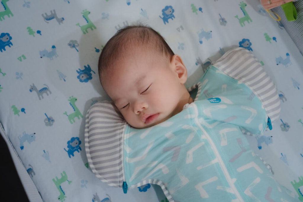 A sleeping baby boy wears a blue Love To Dream stage two in a Chicco Next 2 Me