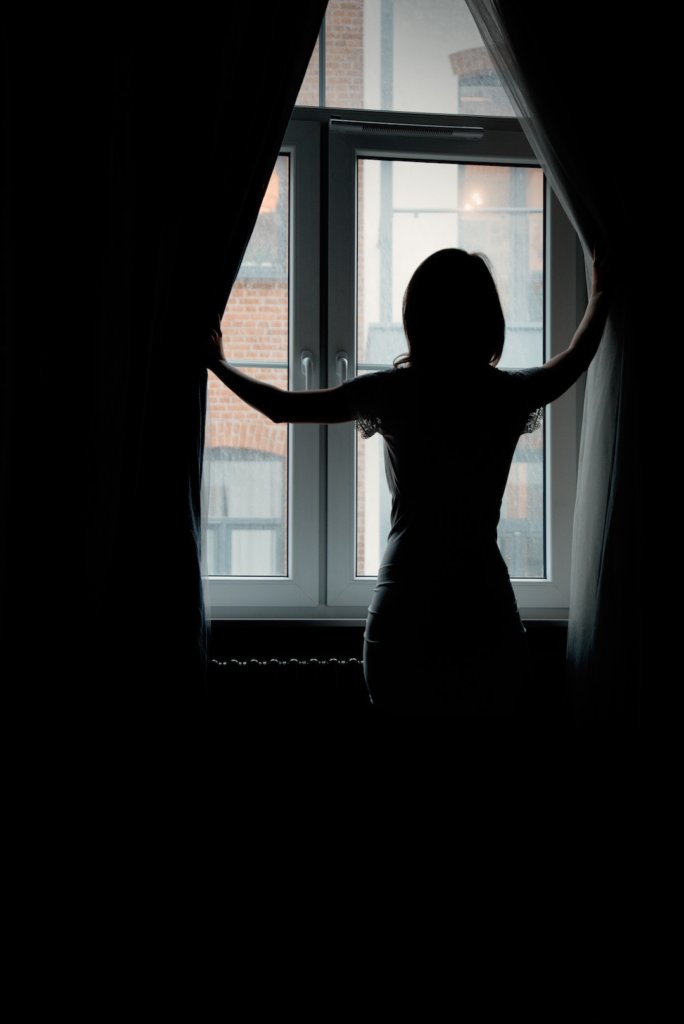 a young girl looks behind the curtains in the window in the morning