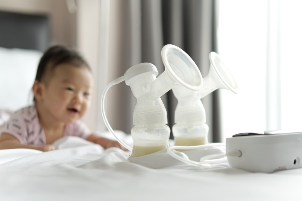 Breast milk in milk pump's bottles and pump machine on the bed with smiling baby crawling in background. The milk got from milk pump's machine and ready for the baby. Baby health care concept.