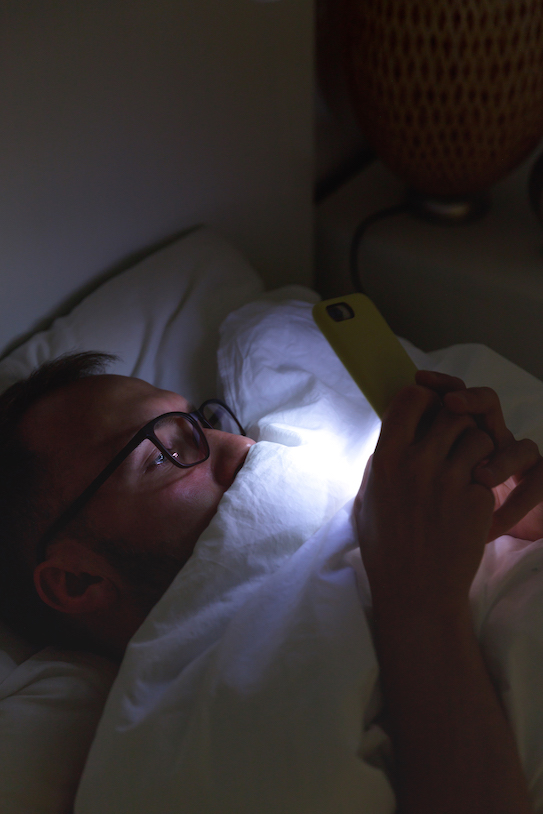 Addiction, nomophobia, insomnia. Close up of sleepy man in glasses using smartphone, lying on bed under the blanket at late night, can not sleep.
